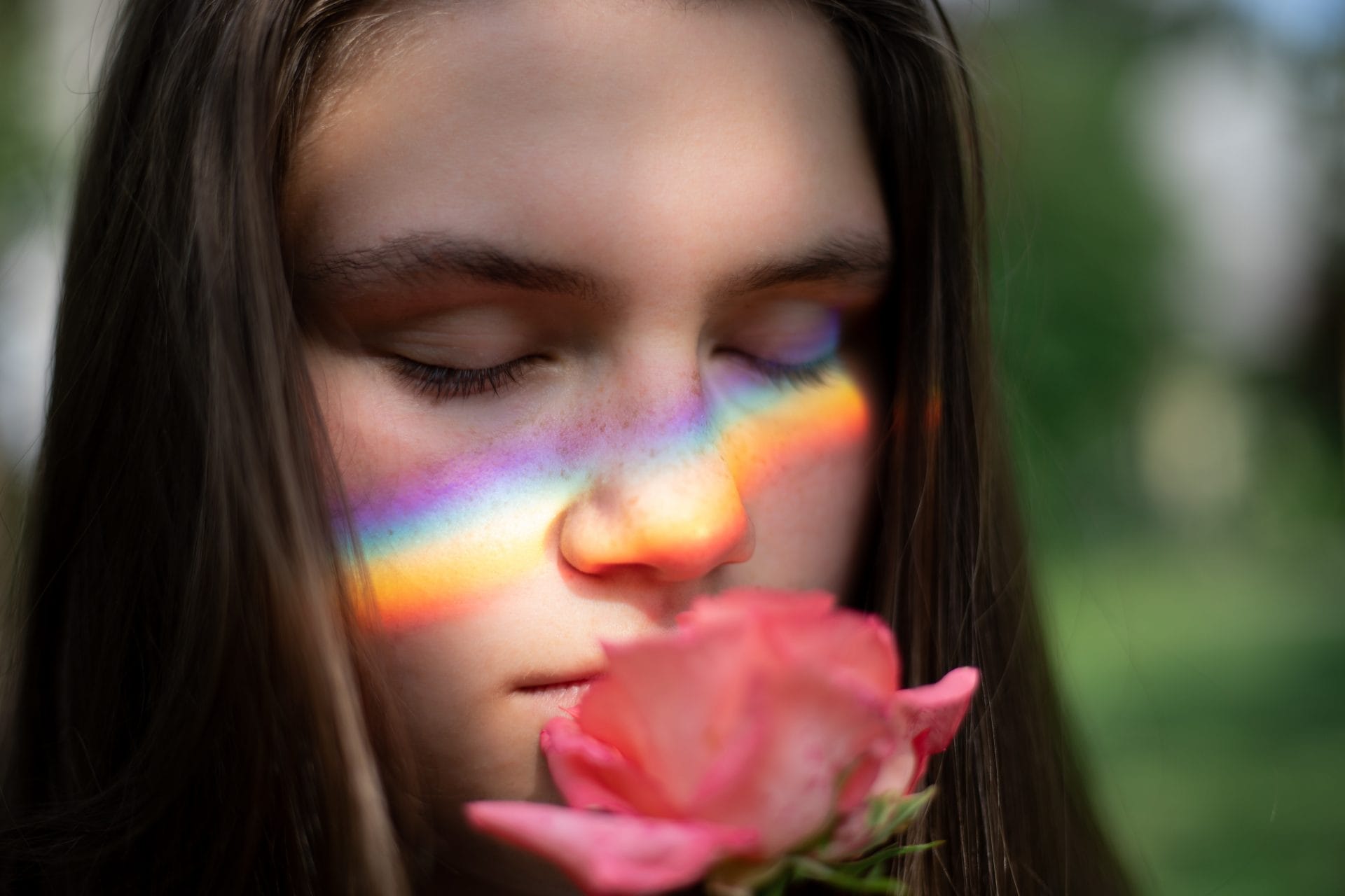 Woman sniffing a rose with a rainbow on her face
